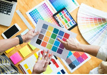 El diseñador discute con un cliente la elección de los colores para el trabajo de pintura que pronto comenzará en Bromont. En la mesa hay varias paletas de colores, un portátil y un teléfono inteligente. 