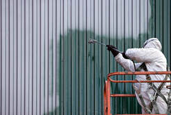 Pintor profesional en Bromont usando equipo de protección total en una góndola. Pinta el revestimiento de un edificio de metal.